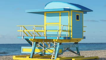 Una torre de salvavidas con una combinación de colores azul y amarillo, situada en una playa arenosa con el océano al fondo.