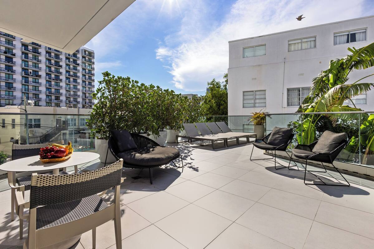 Eine Dachterrasse mit Glasgeländer, Sitzgelegenheiten im Freien und Blick auf ein modernes Gebäude.