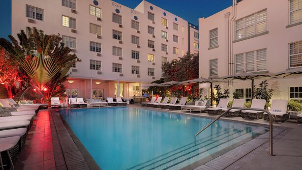 A hotel pool area with lounge chairs and umbrellas, surrounded by a building with multiple windows and balconies. - Park Central South Beach (Miami Beach)