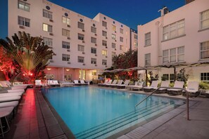 A hotel pool area with lounge chairs and umbrellas, surrounded by a building with multiple windows and balconies. - Park Central South Beach (Miami Beach)
