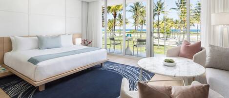 Een hotelkamer met een bed, een ronde tafel en uitzicht op palmbomen en de oceaan.