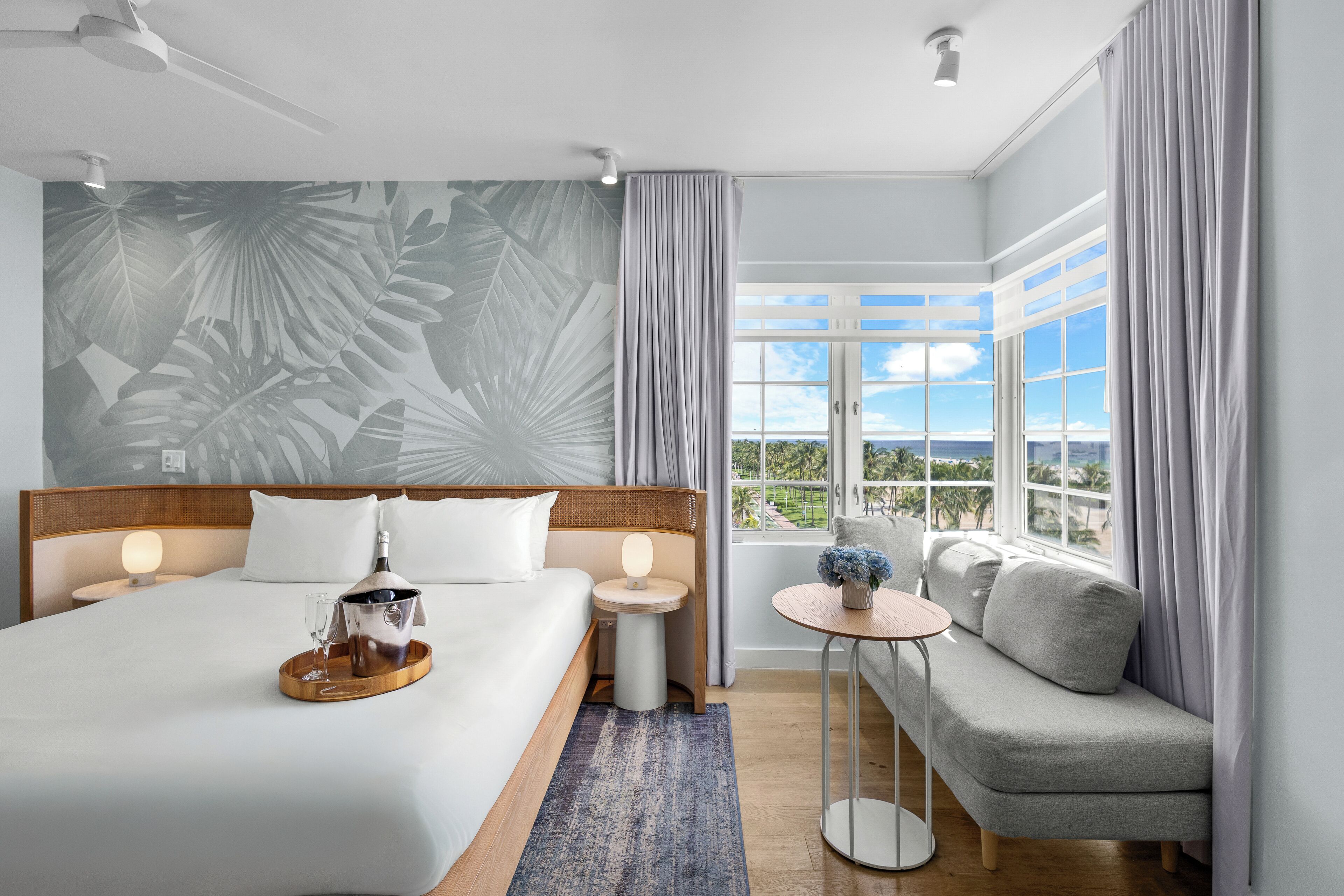 A modern hotel room with a large bed, a small round table, a sofa, and a view of the outdoors.
