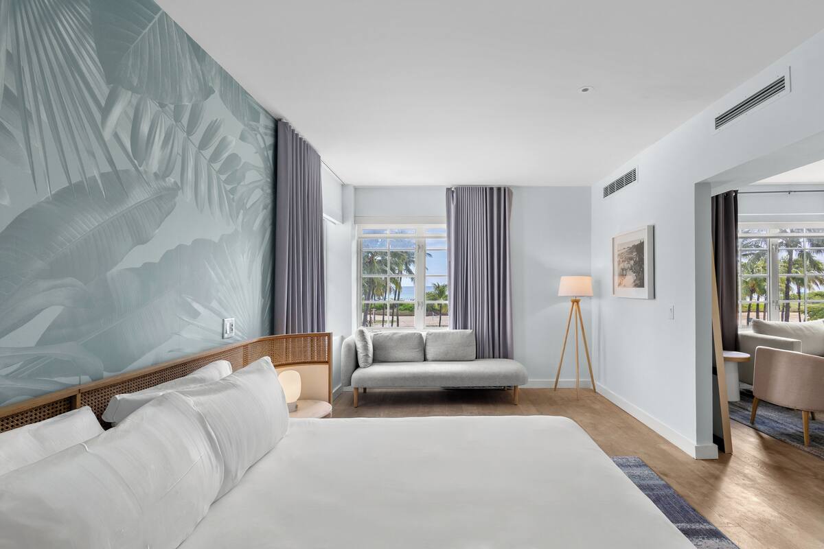 Ein Hotelzimmer mit einem großen Bett, einer Couch, einem kleinen Tisch, einer Lampe und Blick ins Freie.