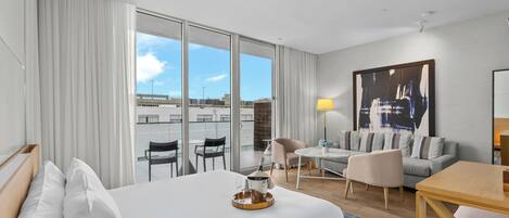 A modern hotel room with a large bed, a dining area, and a sofa.