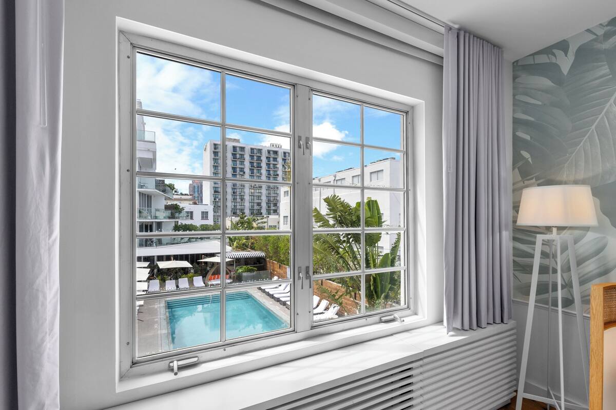 Ein Zimmer mit großem Fenster mit Blick auf einen Pool und Gebäude, einem Heizkörper und einer Lampe.