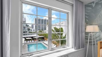 A room with a large window overlooking a pool and buildings, a radiator, and a lamp.