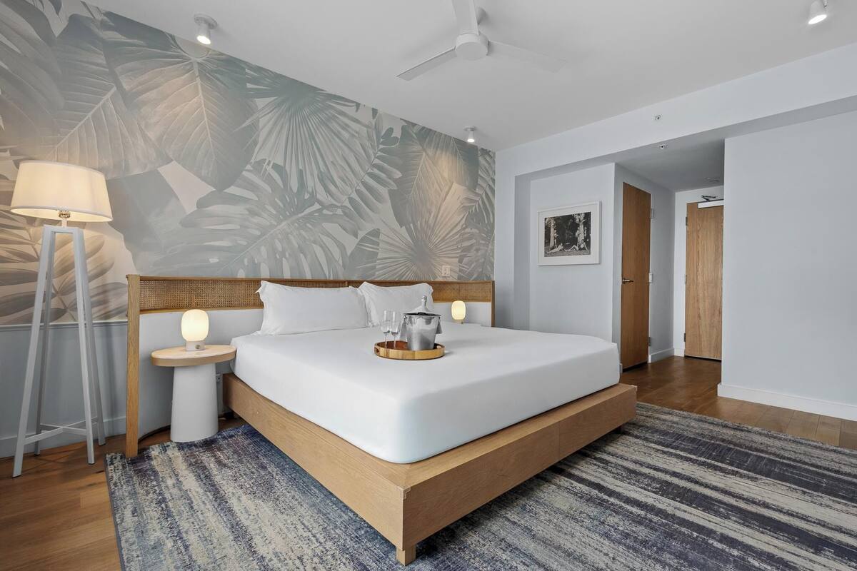 Ein modernes Hotelzimmer mit einem großen Bett, einer Stehlampe, einem Wandbild und einem Deckenventilator.