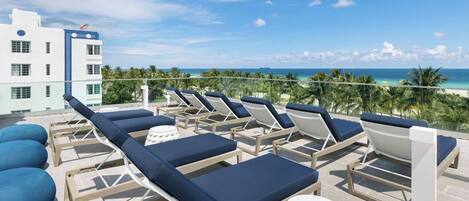 A rooftop lounge area with sun loungers and a view of the ocean.