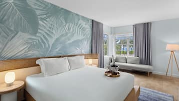 A hotel room with a large bed, a sofa, a lamp, and a view of the outdoors.