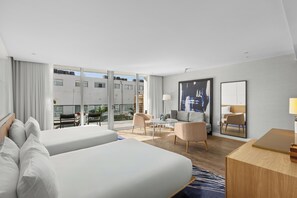 Une chambre d’hôtel avec deux lits, un coin salon comprenant une chaise et une table, une grande fenêtre et un miroir au mur.