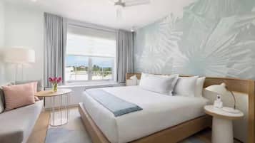 A modern hotel room with a large bed, a small table, a nightstand, and a view of the outdoors.