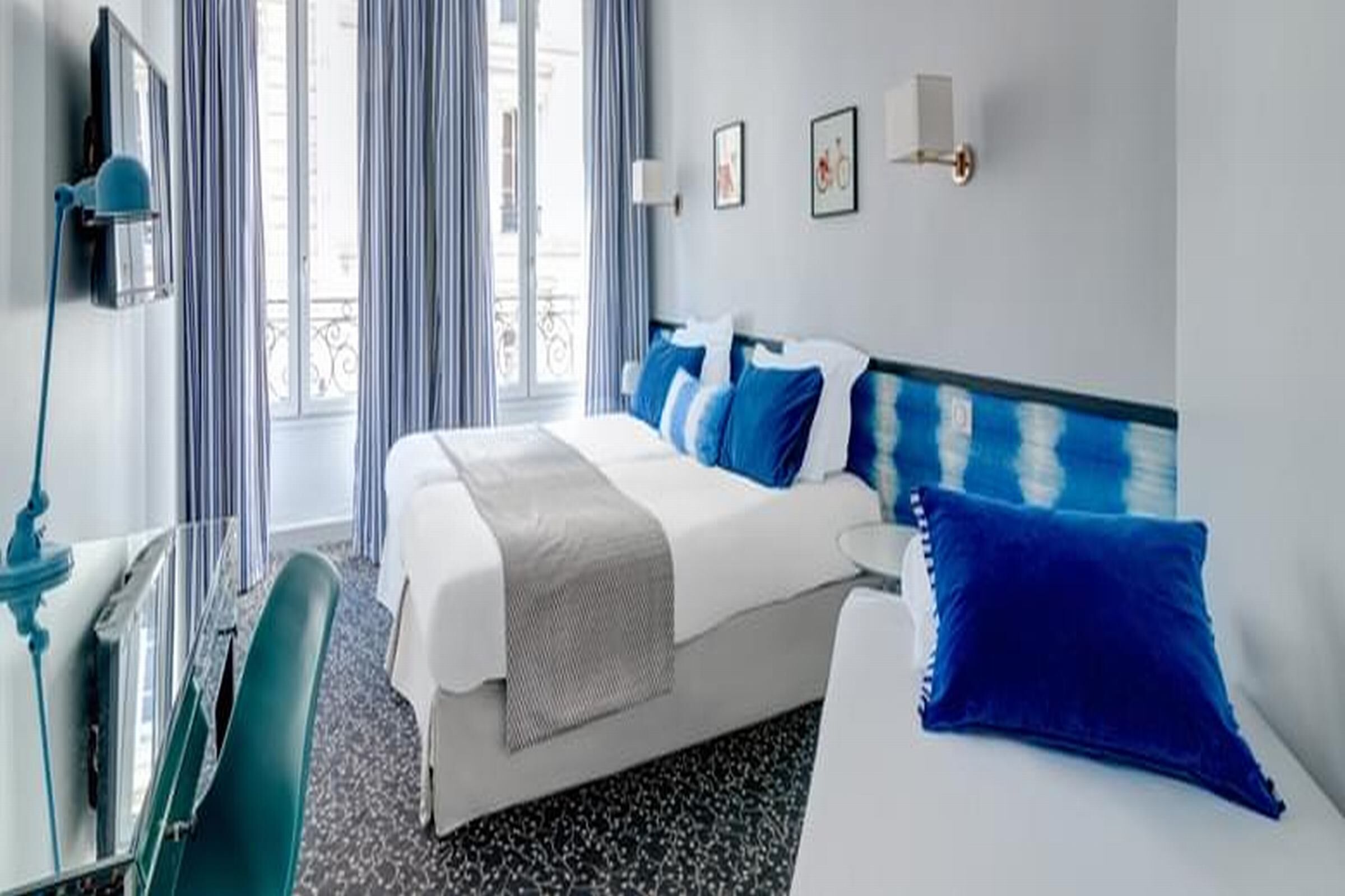 A hotel room with a bed, a desk, a chair, a TV, and a window with curtains.