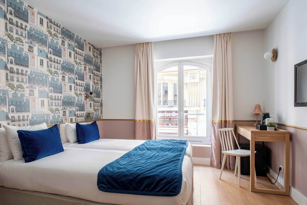 Habitación de hotel con una cama grande, un escritorio y vistas a la ciudad a través de una ventana.