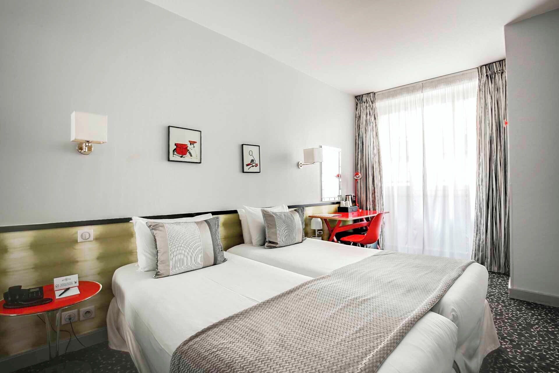 A hotel room with two beds, a desk, a chair, a telephone, and a window with curtains.