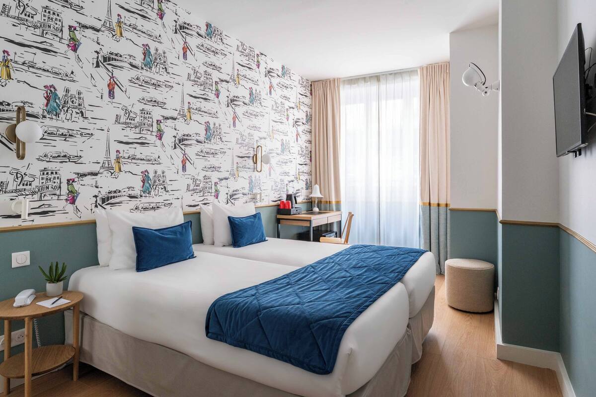 Habitación de hotel con dos camas, un escritorio, una silla, una lámpara, un televisor y una ventana con cortinas.