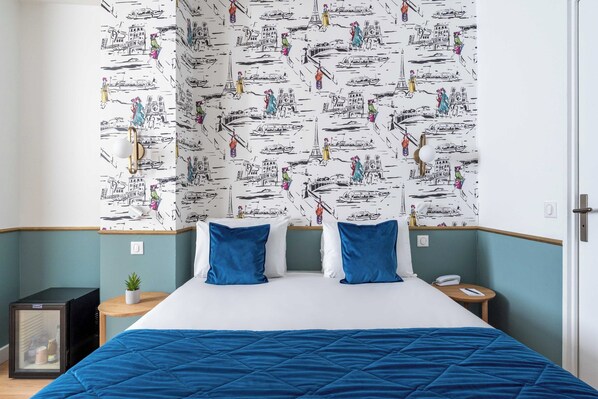 A hotel room with a bed, two pillows, a small table, a nightstand, a refrigerator, and a wall with a patterned design. - Hôtel Acadia - Astotel (Paris)