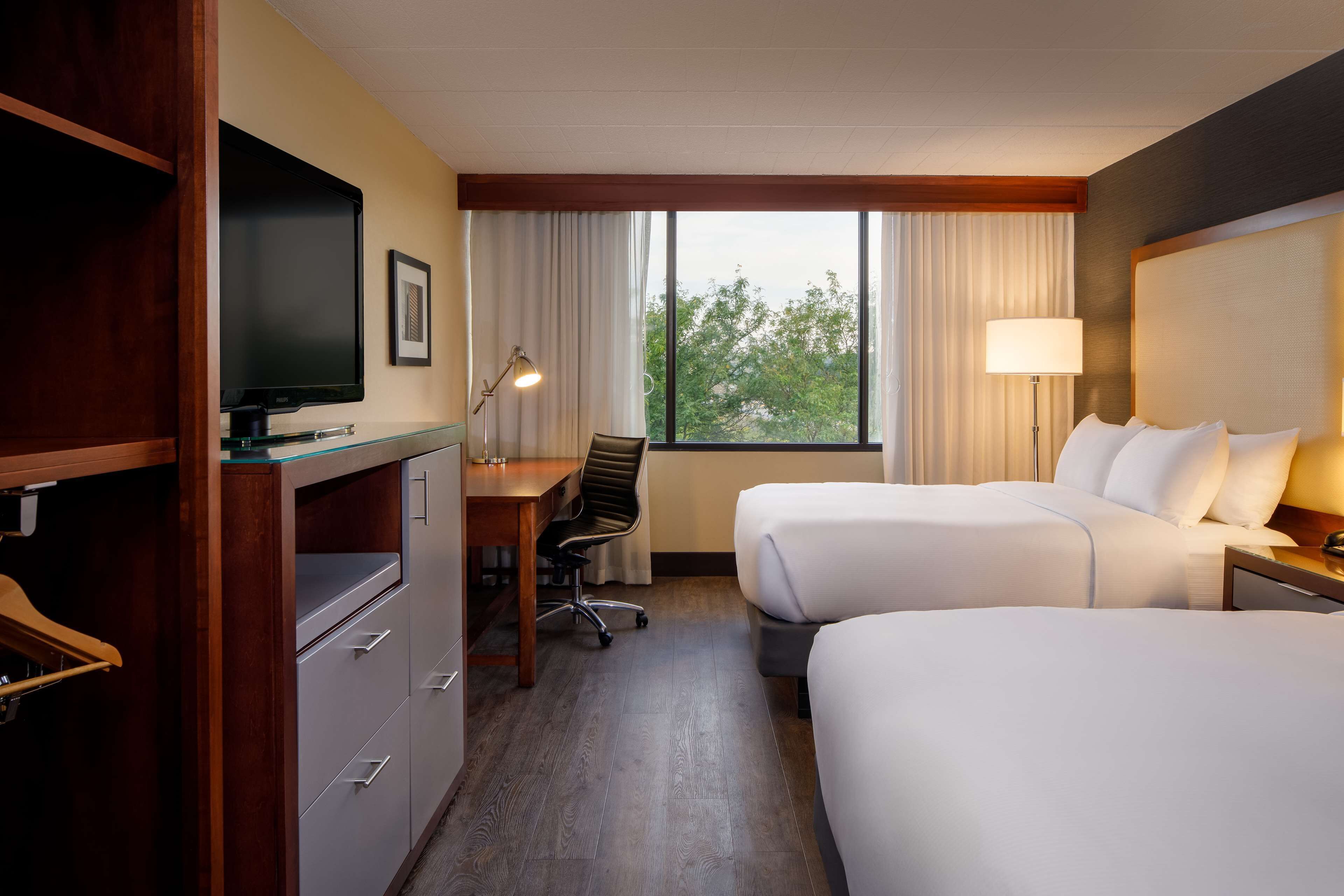 Habitación de hotel con dos camas, un escritorio con silla, televisor y ventana con cortinas.