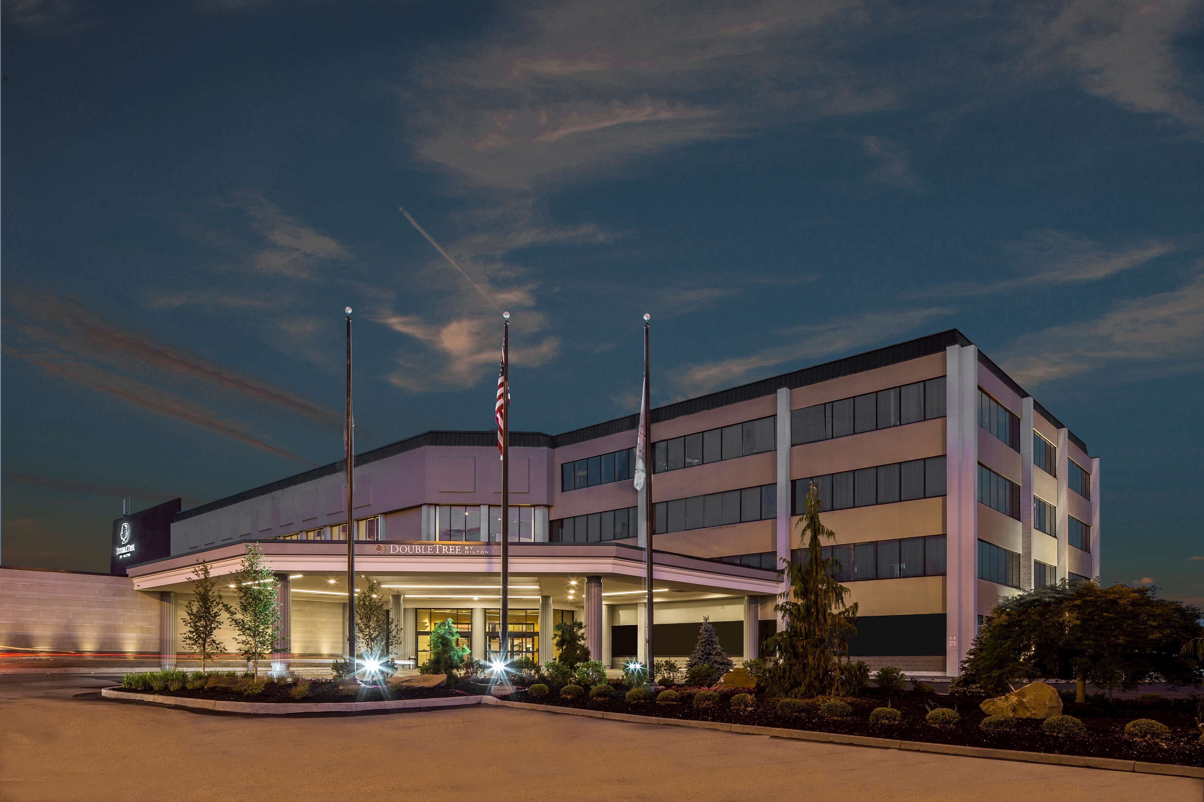 A modern hotel with a prominent entrance, flagpoles, and a well-lit facade.