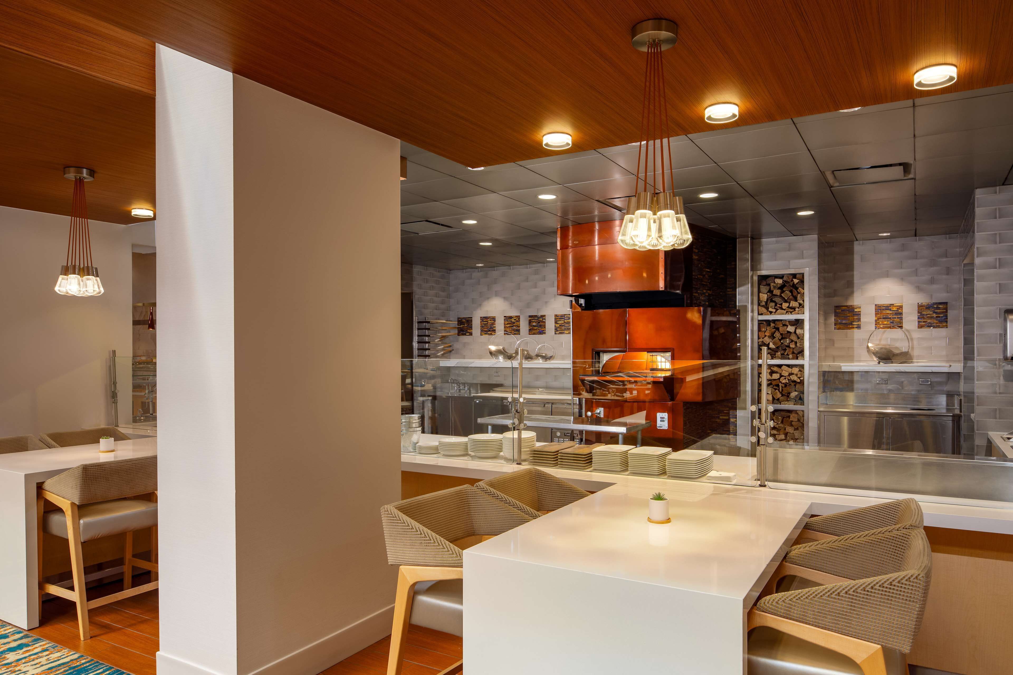 Un intérieur de restaurant moderne avec un espace de restauration central, un plafond en bois et des luminaires suspendus.