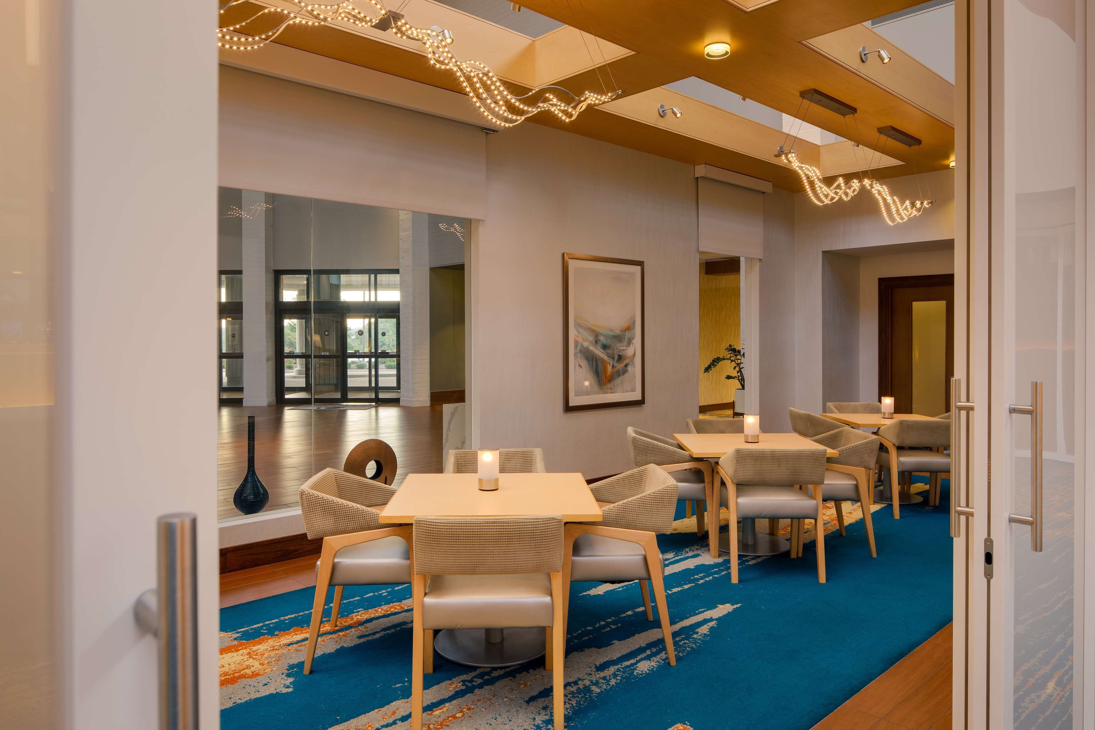 Un espace de restauration moderne dans un hôtel, avec des tables et des chaises, une moquette bleue et un éclairage décoratif.