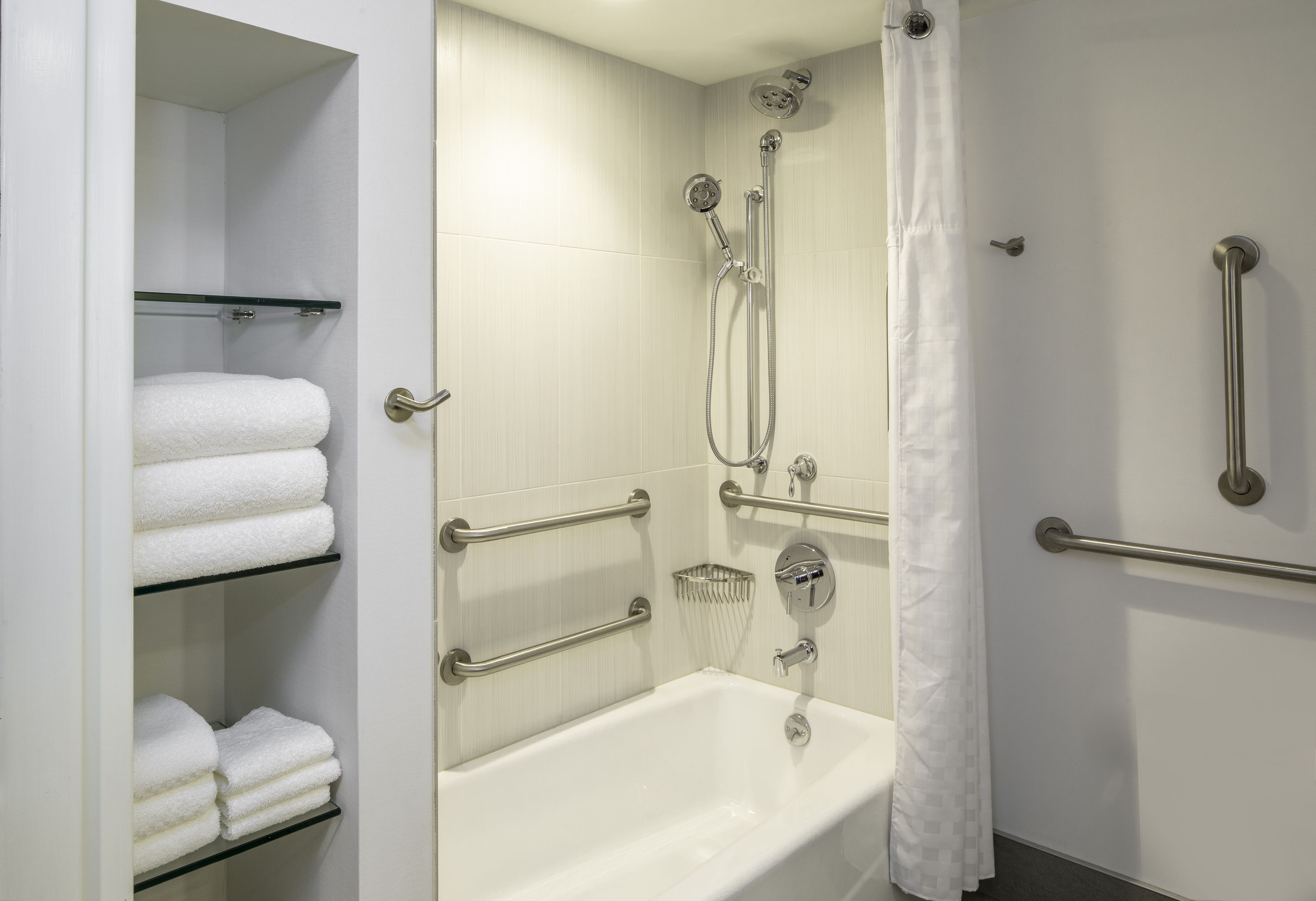 Une salle de bain avec une baignoire blanche, une douche équipée d’un pommeau de douche à main et un porte-serviettes avec des serviettes pliées.