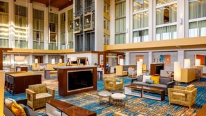 A spacious lobby with multiple seating areas, a large TV screen, and a high ceiling with large windows. - DoubleTree by Hilton Pittsburgh - Cranberry (Mars)