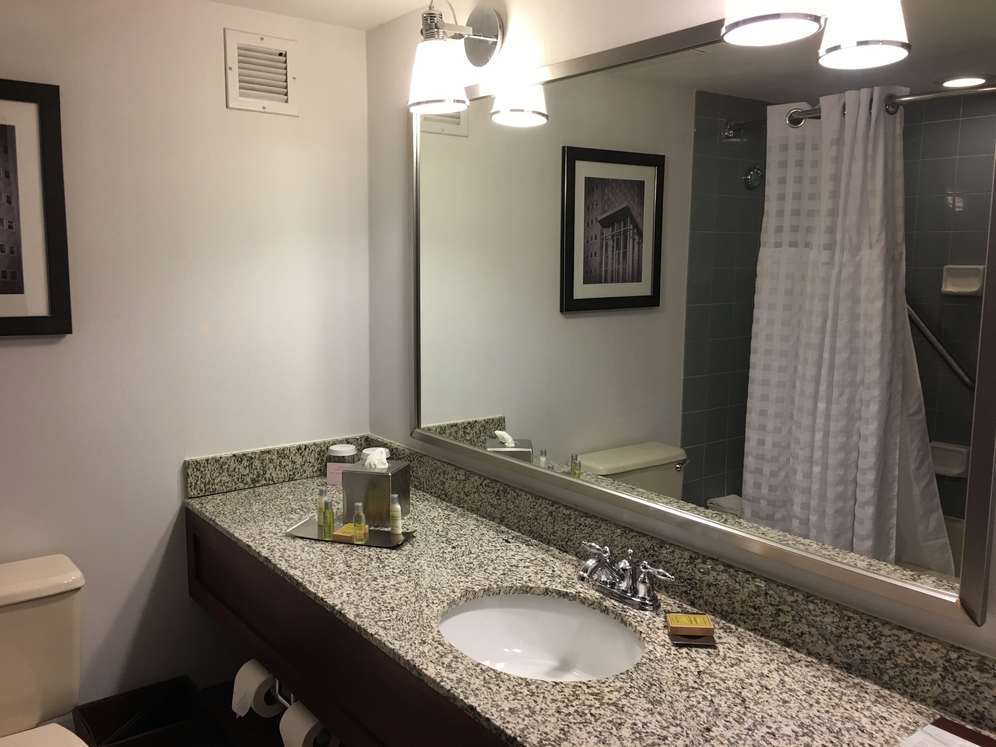 A bathroom with a granite countertop, a sink, a mirror, and a shower curtain.