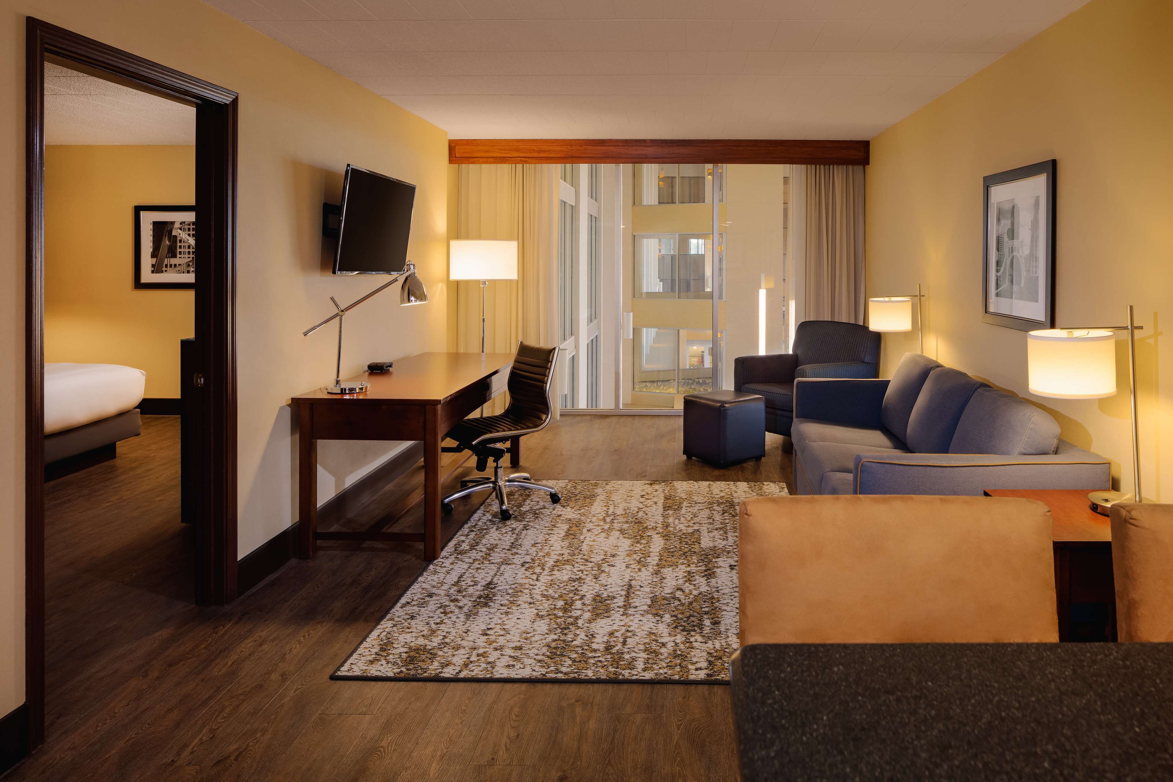 A hotel room with a bed, a desk, a chair, a sofa, and a TV.