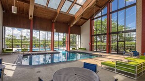 A swimming pool area with a glass ceiling, large windows, and outdoor seating. - DoubleTree by Hilton Pittsburgh - Cranberry (Mars)
