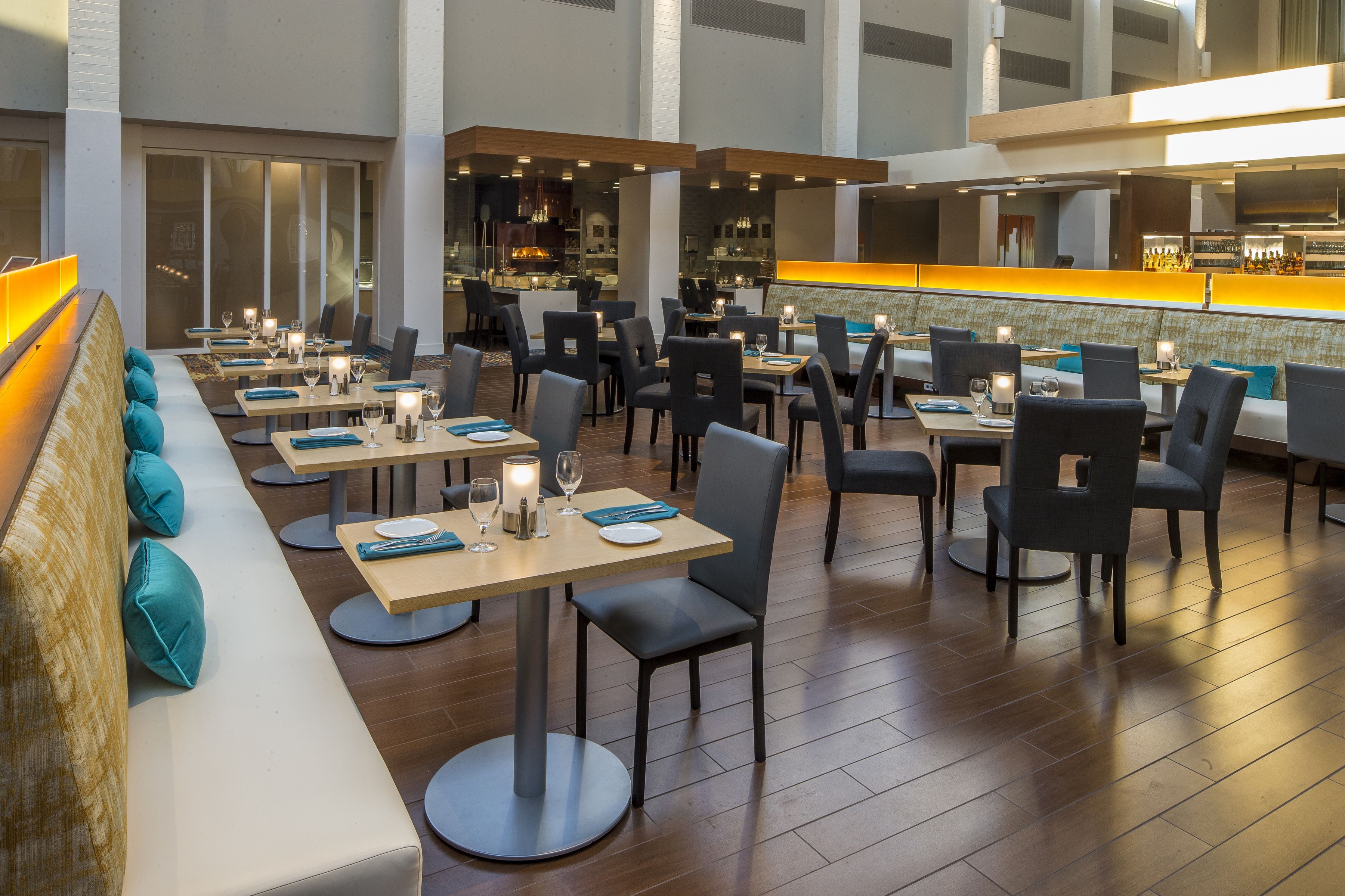 A modern restaurant with multiple dining tables and chairs, a bar area, and a seating section with a cushioned bench.