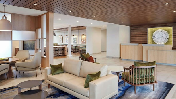 A modern lobby with a sofa, chairs, a reception desk, and a dining area. - Fairfield by Marriott Inn & Suites Matteson Chicago (Matteson)