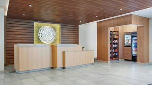 A reception area with a wooden reception desk, a wall-mounted decorative piece, and a vending machine. - Fairfield by Marriott Inn & Suites Matteson Chicago (Matteson)