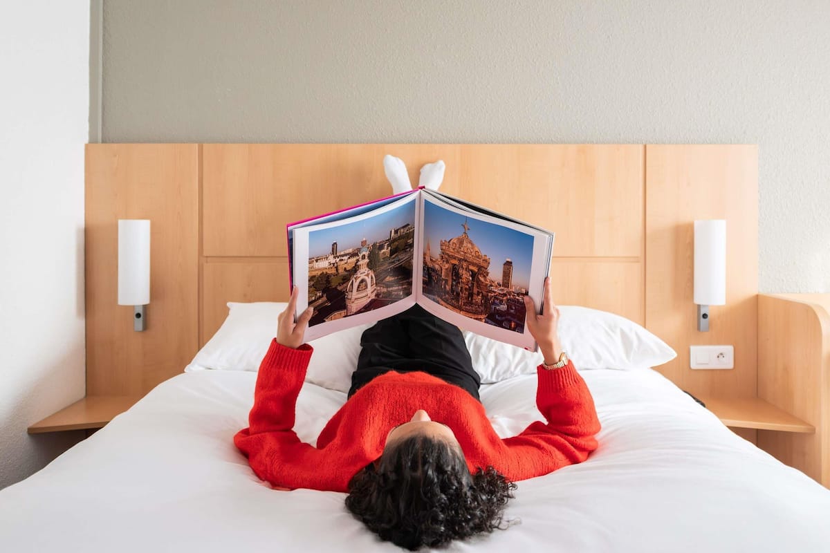 Una persona recostada en una cama leyendo un libro.