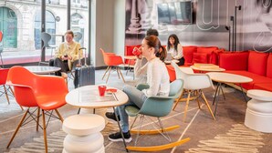 Un espace lounge moderne avec des tables rondes, des fauteuils orange et turquoise, et un canapé rouge.