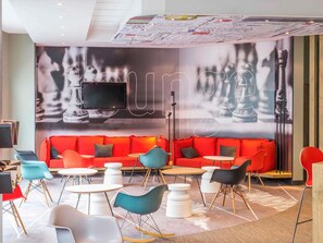 Un espace de détente moderne avec un canapé rouge, des fauteuils bleu sarcelle et noirs, et un grand téléviseur fixé au mur.