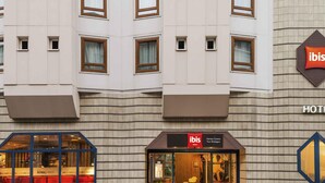 La façade d’un hôtel, ornée de nombreuses fenêtres, affiche une enseigne « ibis » bien visible et une entrée clairement identifiable grâce à une porte en verre.