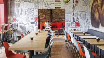 Un comedor moderno con una larga mesa de madera, sillas coloridas y un sofá rojo. Las paredes están decoradas con diversas inscripciones y dibujos.