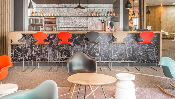 Un espace bar moderne avec un mur aux motifs noir et blanc, des tabourets de bar rouges et une variété de bouteilles exposées sur des étagères.