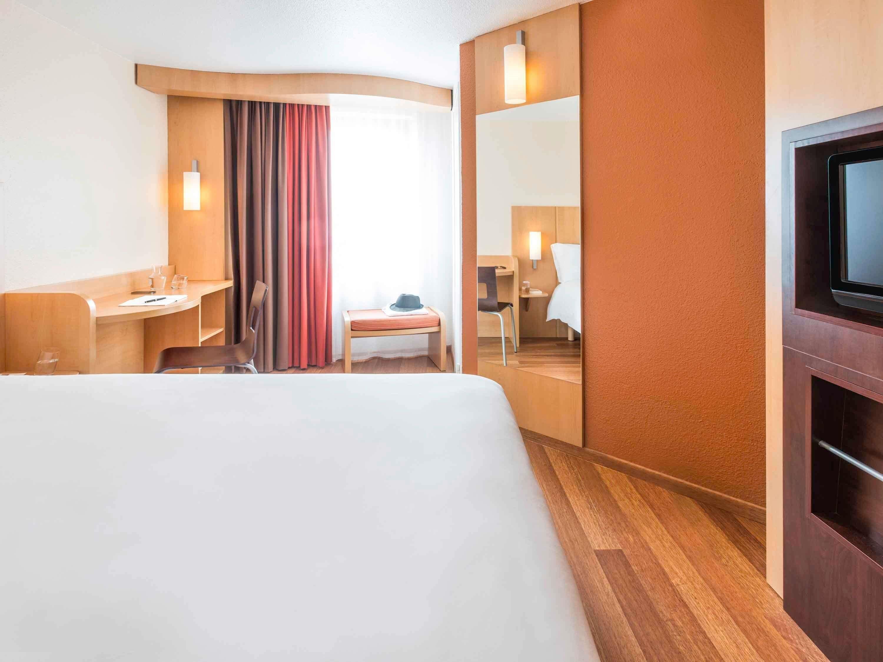 A hotel room with a large bed, a desk, a chair, a small table, and a television.