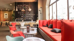 Un espace de détente moderne avec un canapé rouge, des fauteuils colorés et un tableau noir sur lequel sont écrits des mots liés au monde des affaires.