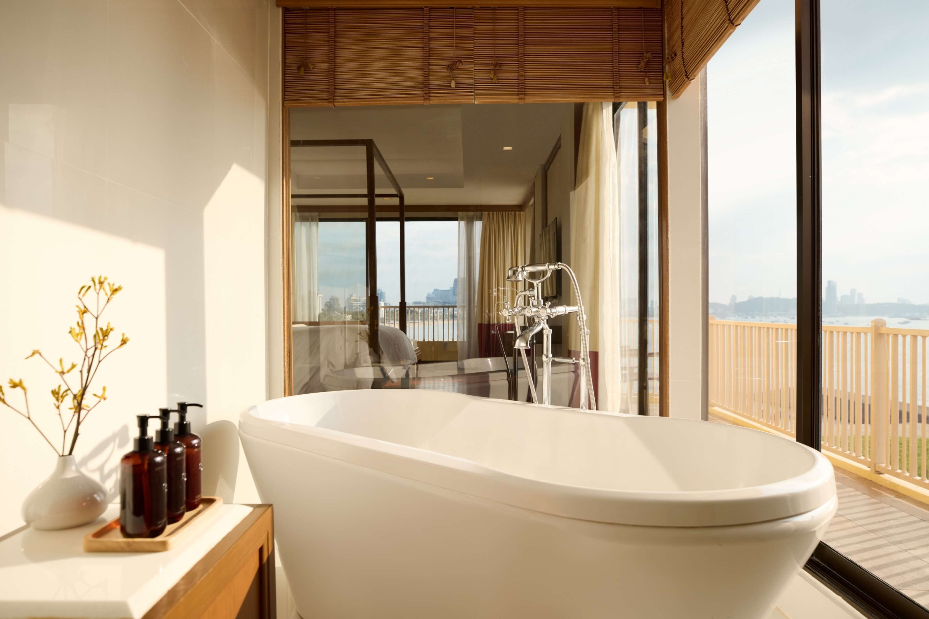 A modern bathroom with a freestanding bathtub, a vanity with toiletries, and a large window offering a city view.