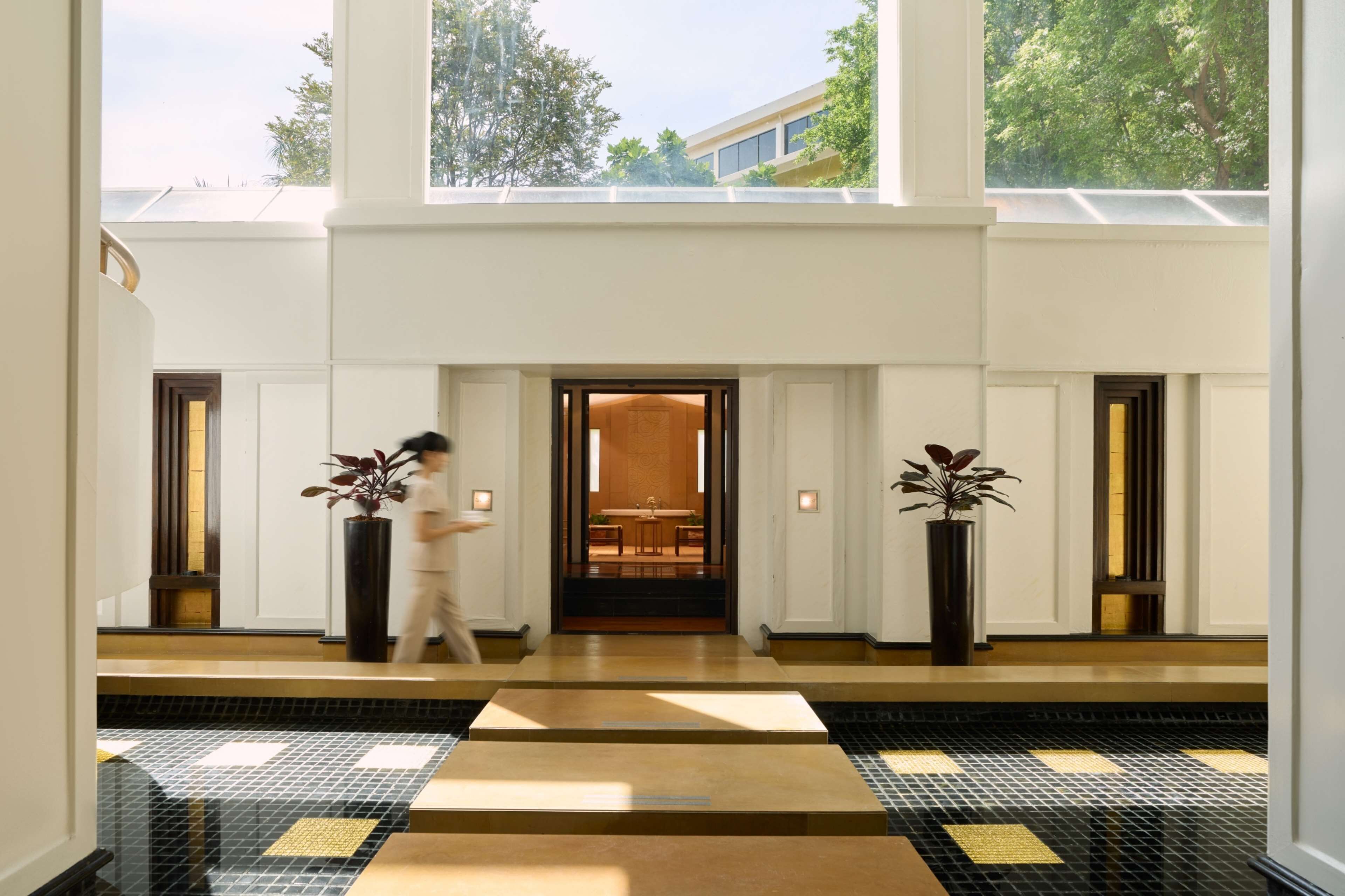 Un vestíbulo espacioso con techo alto, ventanas grandes y piso de baldosas que conduce a una zona de recepción.