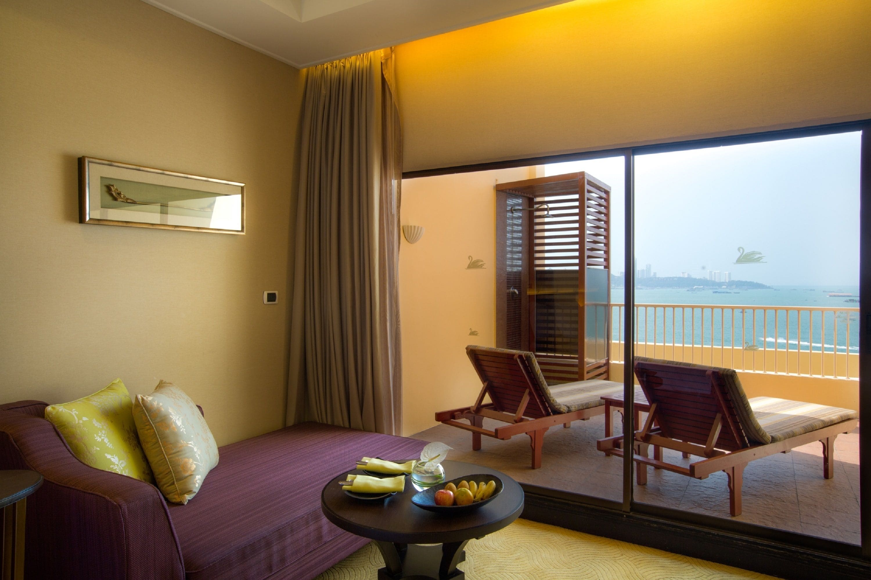 A hotel room with a balcony, a bed, a table with fruits, and a view of the sea.