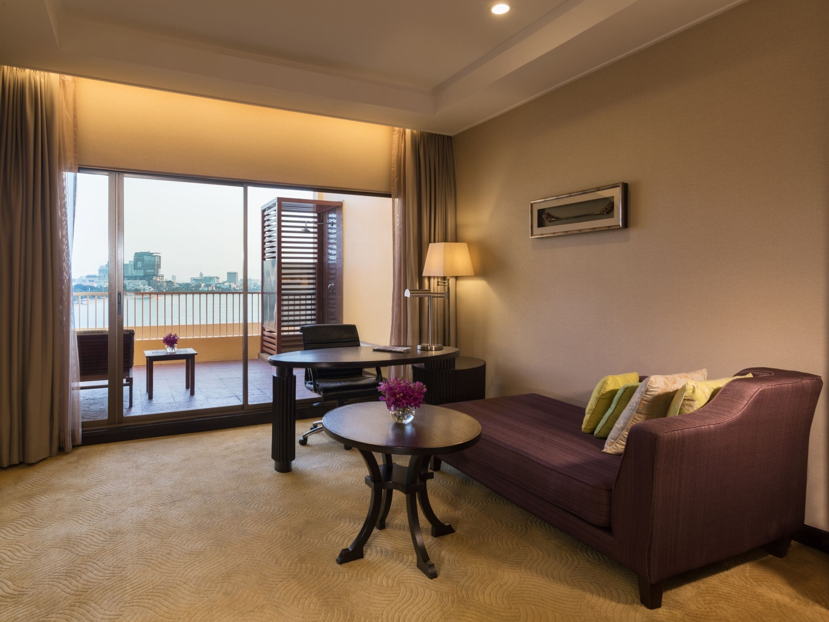 Una habitación de hotel con balcón, sofá, mesa y lámpara.