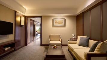 A living room with a flat-screen TV, a sofa, a chair, and a coffee table with fruit.