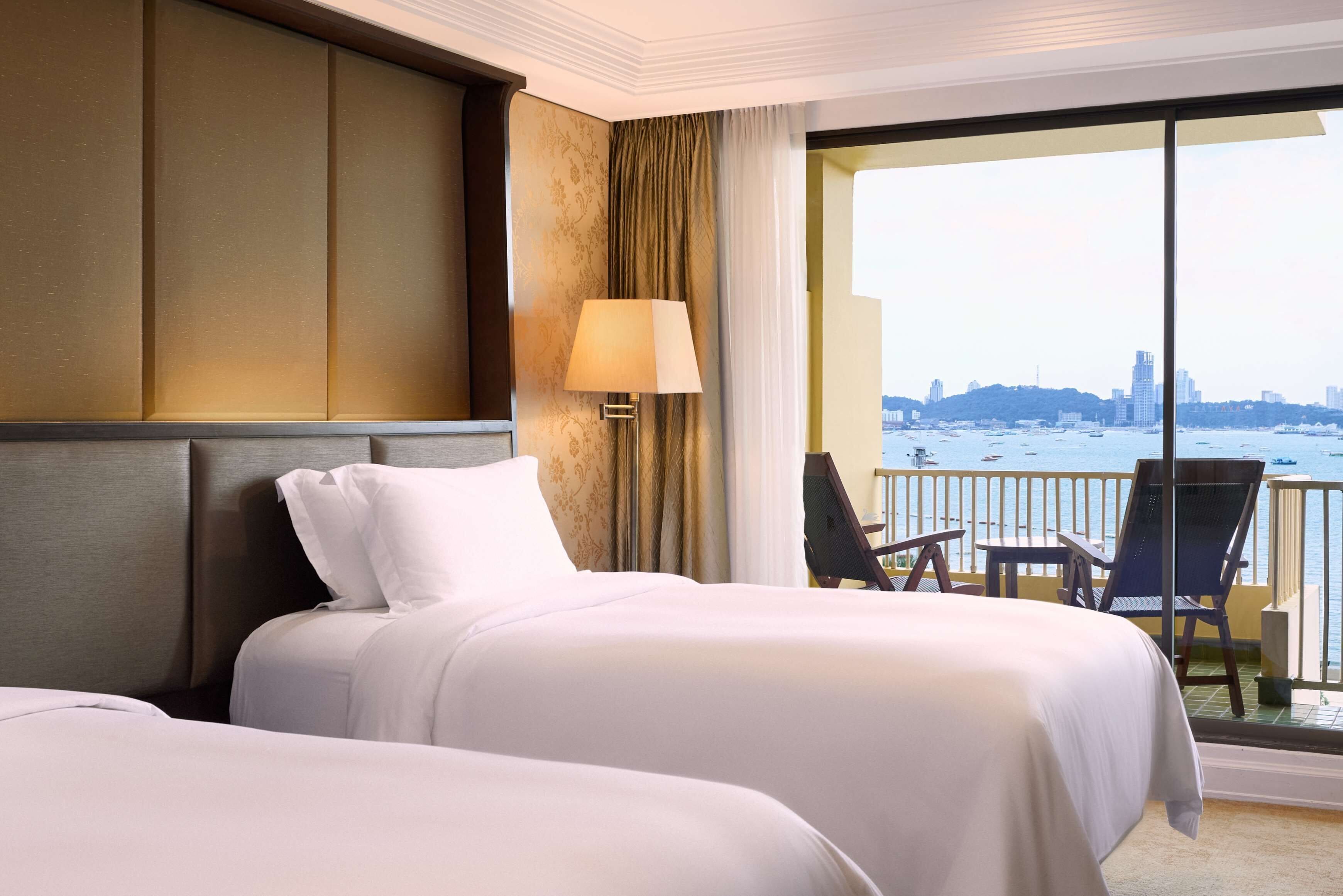 Habitación de hotel con dos camas, vista a la ciudad y balcón con sillas.