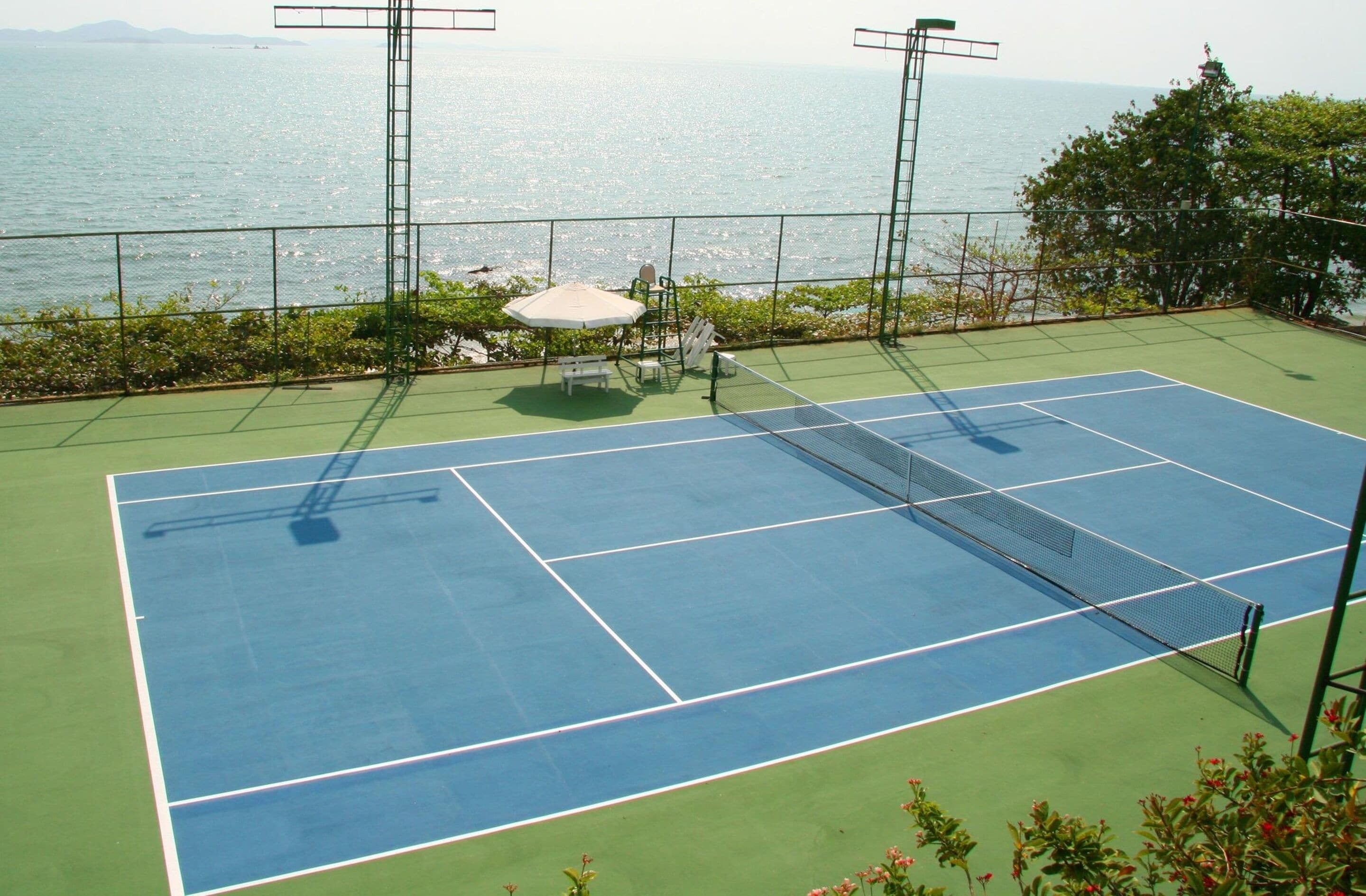 Una cancha de tenis con una red, rodeada por una valla, con vistas a un cuerpo de agua.