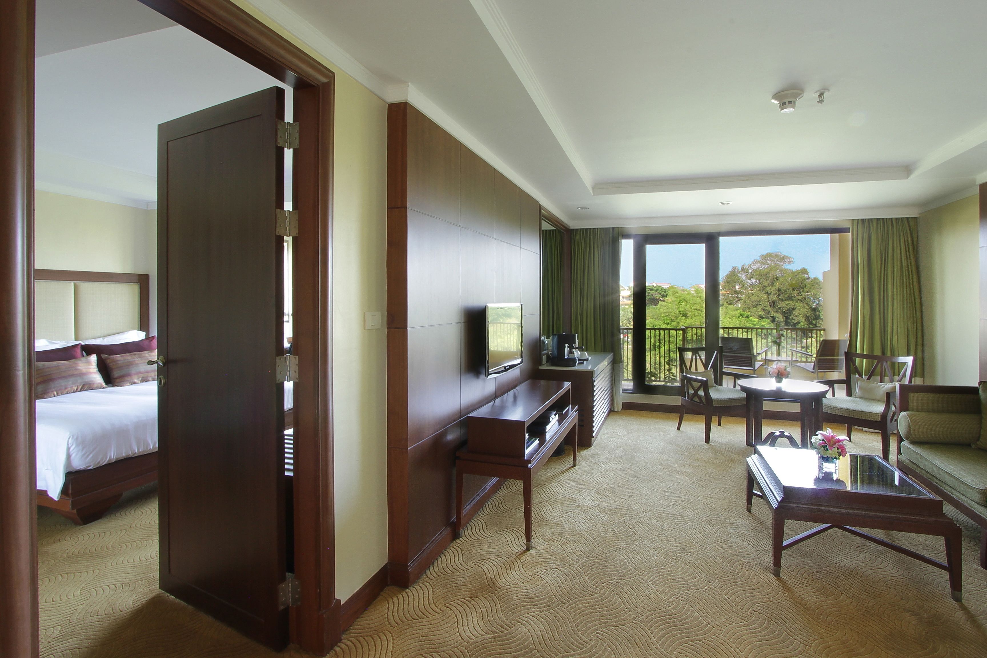 A hotel room with a bed, a TV, a desk, a sofa, and a balcony with a view.