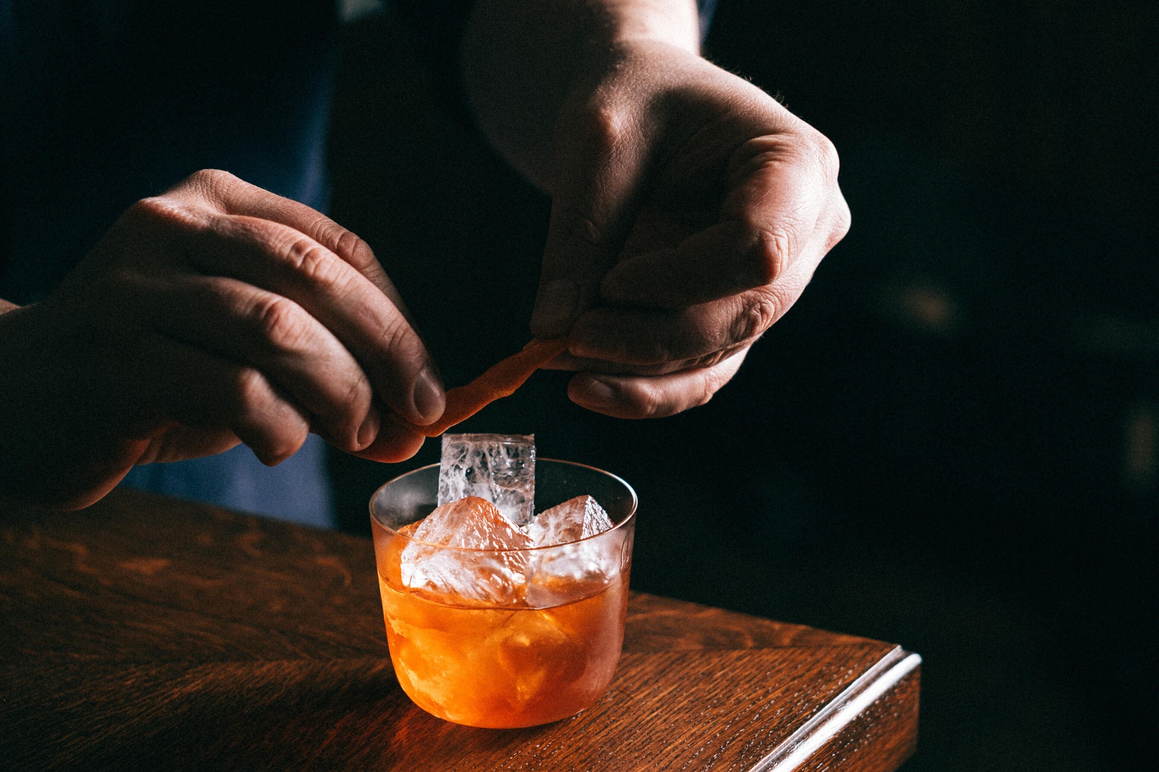A person holding a spoon over a glass with ice cubes.