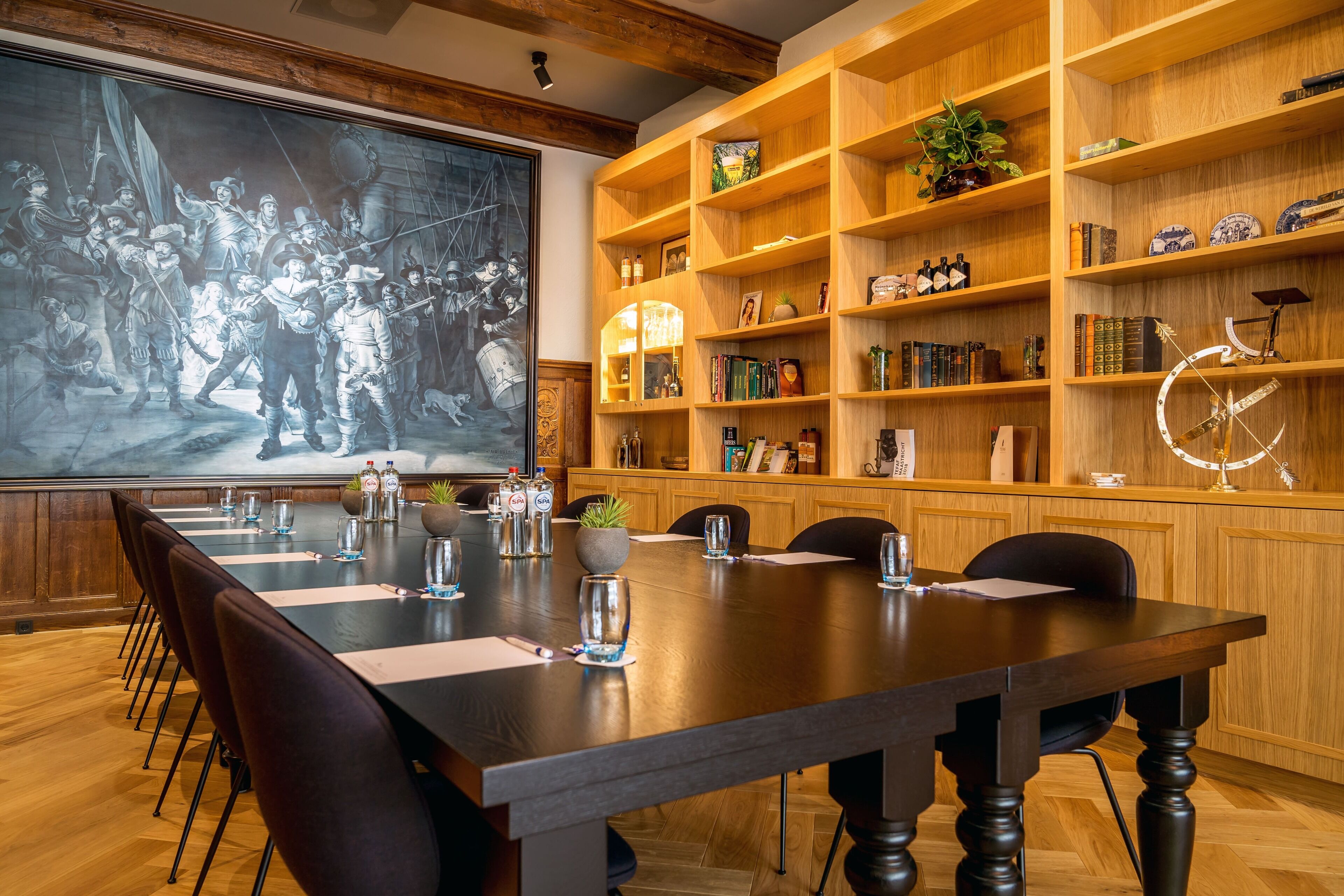 A conference room with a long table, chairs, a projector screen, and wooden shelves with books and decorative items.